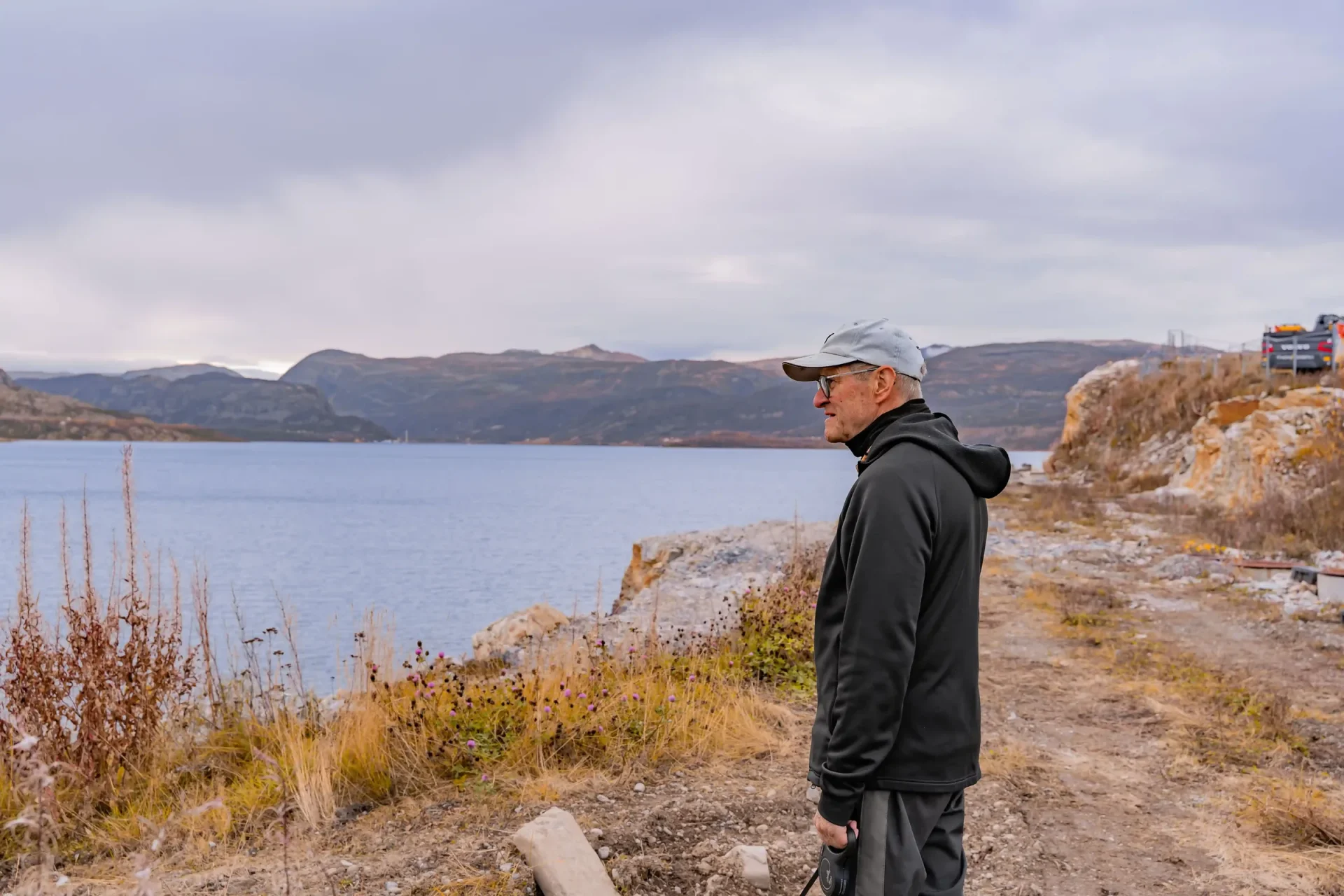Kjell står i profil på stien langs sjøen og ser utover Altafjorden, med fjellene på andre siden av fjorden.