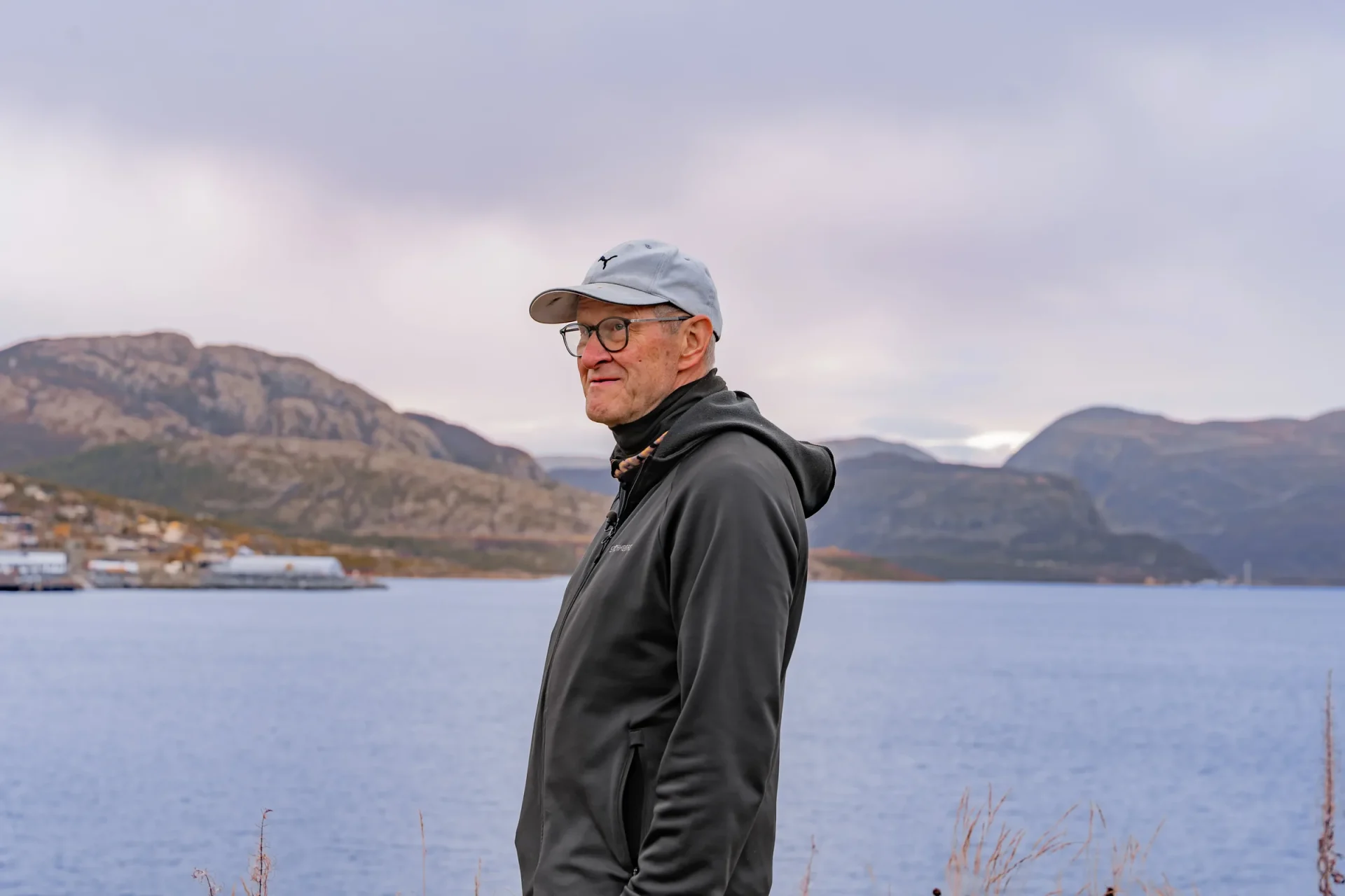 Kjell i profil ved sjøen, med Altafjorden, havneområdet i Alta og fjellene i bakgrunnen.